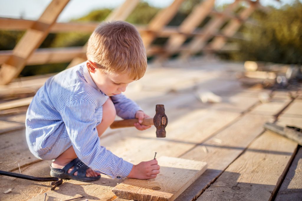 Kind hammert mit Hammer Nägel in Holz