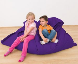 Zwei Kinder sitzen entspannt auf einem lila Sitzsack in einem hellen Raum mit Holzboden.