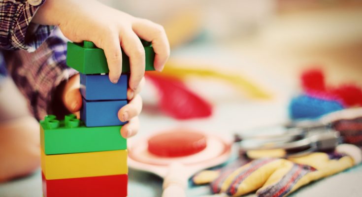 Eine Kleinkindhand baut mit Lego Duplo einen Turm.