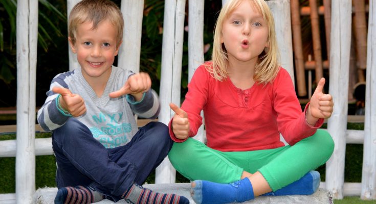 Zwei Kinder sitzen lächelnd nebeneinander und halten die Daumen hoch.