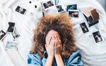 Frau bedeckt ihr Gesicht, während um sie herum Fotos verstreut liegen: Ein Visionboard braucht konkrete Bilder.