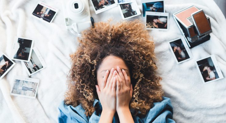 Frau bedeckt ihr Gesicht, während um sie herum Fotos verstreut liegen: Ein Visionboard braucht konkrete Bilder.