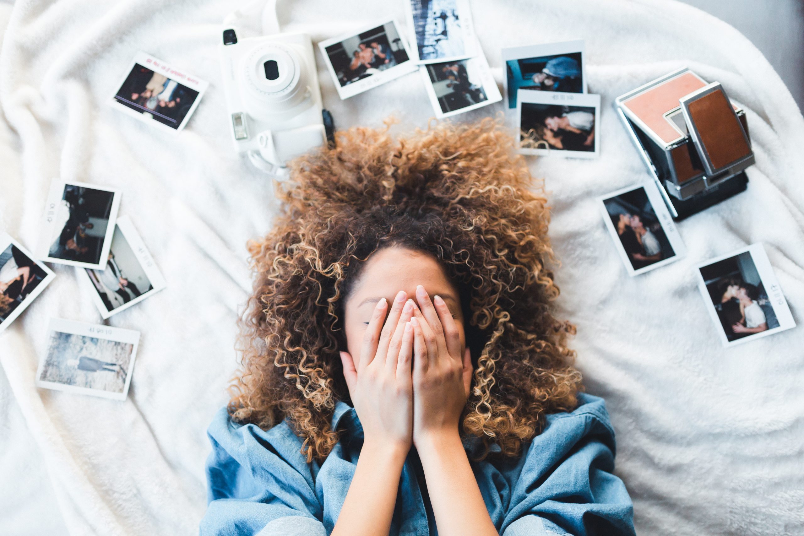 Frau bedeckt ihr Gesicht, während um sie herum Fotos verstreut liegen: Ein Visionboard braucht konkrete Bilder.