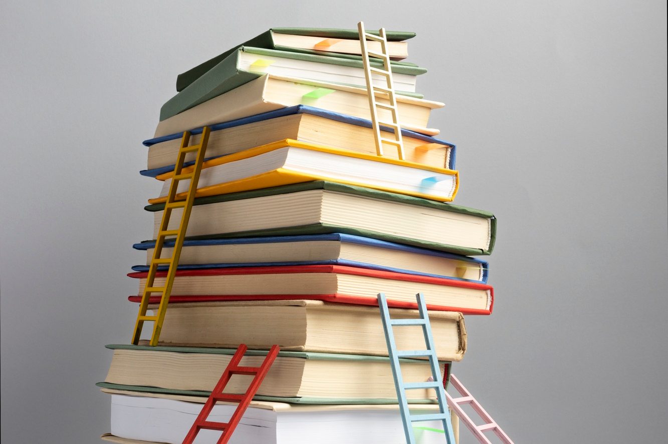 Ein Stapel farbiger Bücher mit kleinen Leitern, die symbolisch den Zugang zu Wissen und Bildung darstellen. Die Bücher sind in verschiedenen Größen und Farben angeordnet, was eine kreative und ansprechende Darstellung von Lernmaterialien zeigt.