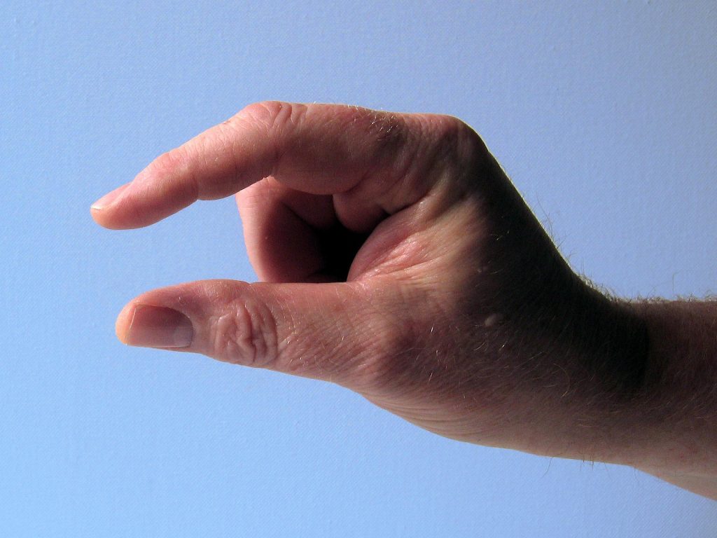 Eine Hand, die eine kleine Menge symbolisiert, zeigt die Finger in einer Greifbewegung. Der Hintergrund ist ein sanftes Blau, das die Geste betont.