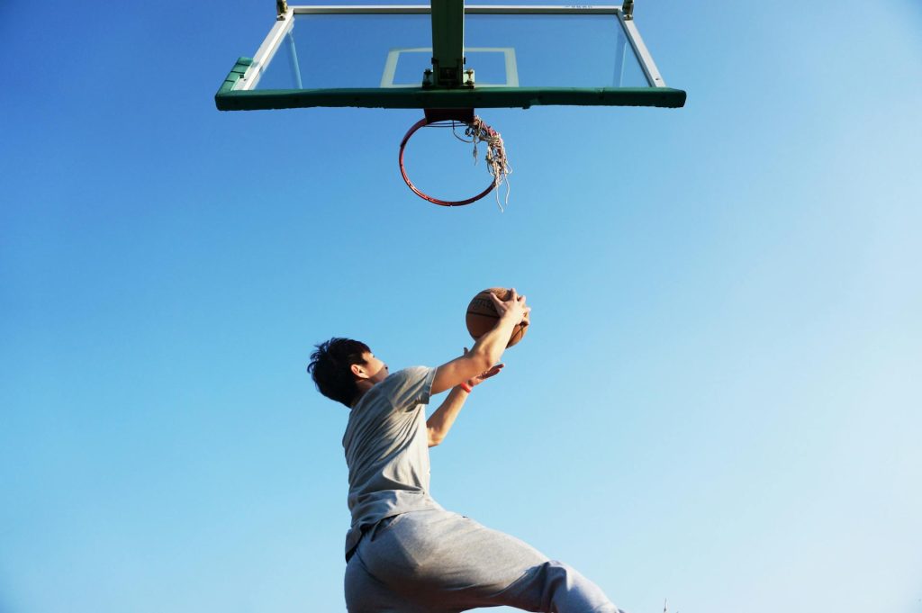 Junger Mann beim Basketballspielen, der einen Wurf in Richtung Korb macht, vor einem klaren blauen Himmel.