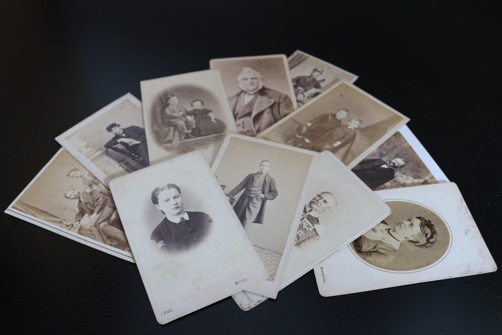 Eine Sammlung historischer Fotografien aus dem 19. Jahrhundert, die verschiedene Porträts von Männern, Frauen und Kindern zeigt. Die Bilder sind auf einem dunklen Tisch angeordnet und vermitteln einen nostalgischen Eindruck vergangener Zeiten.