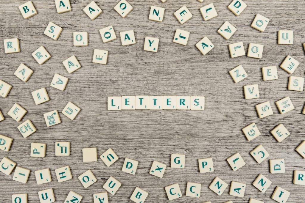 Ein Arrangement von Scrabble-Buchstaben auf einem Holzuntergrund, mit dem Wort "LETTERS" in der Mitte. Die Buchstaben sind in verschiedenen Positionen verteilt und zeigen eine kreative Anordnung. Ideal für Themen wie Spiele, Bildung oder Sprachentwicklung.