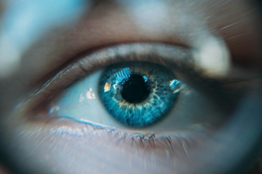 Nahaufnahme eines menschlichen Auges mit leuchtend blauen Farben und feinen Details der Iris. Die Reflexionen im Auge deuten auf eine helle Umgebung hin.