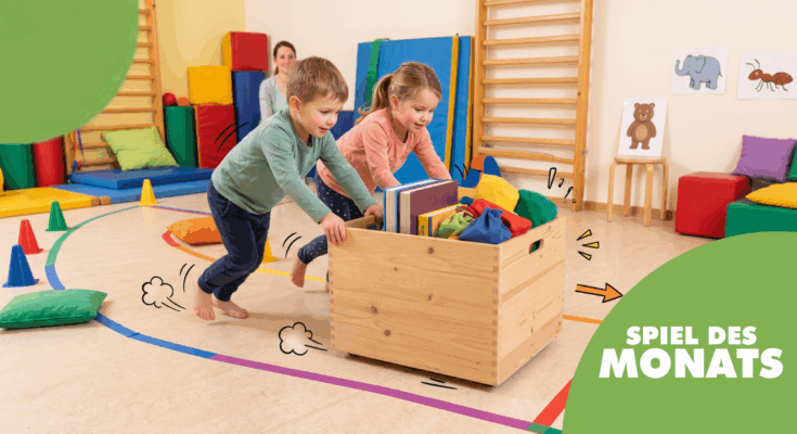 Zwei Kinder spielen in einem bunten Spielraum und schieben eine Holzkiste voller Bücher und Spielzeug. Der Raum ist mit weichen Matten und bunten Kissen ausgestattet, ideal für kreative Aktivitäten und Bewegungsspiele.