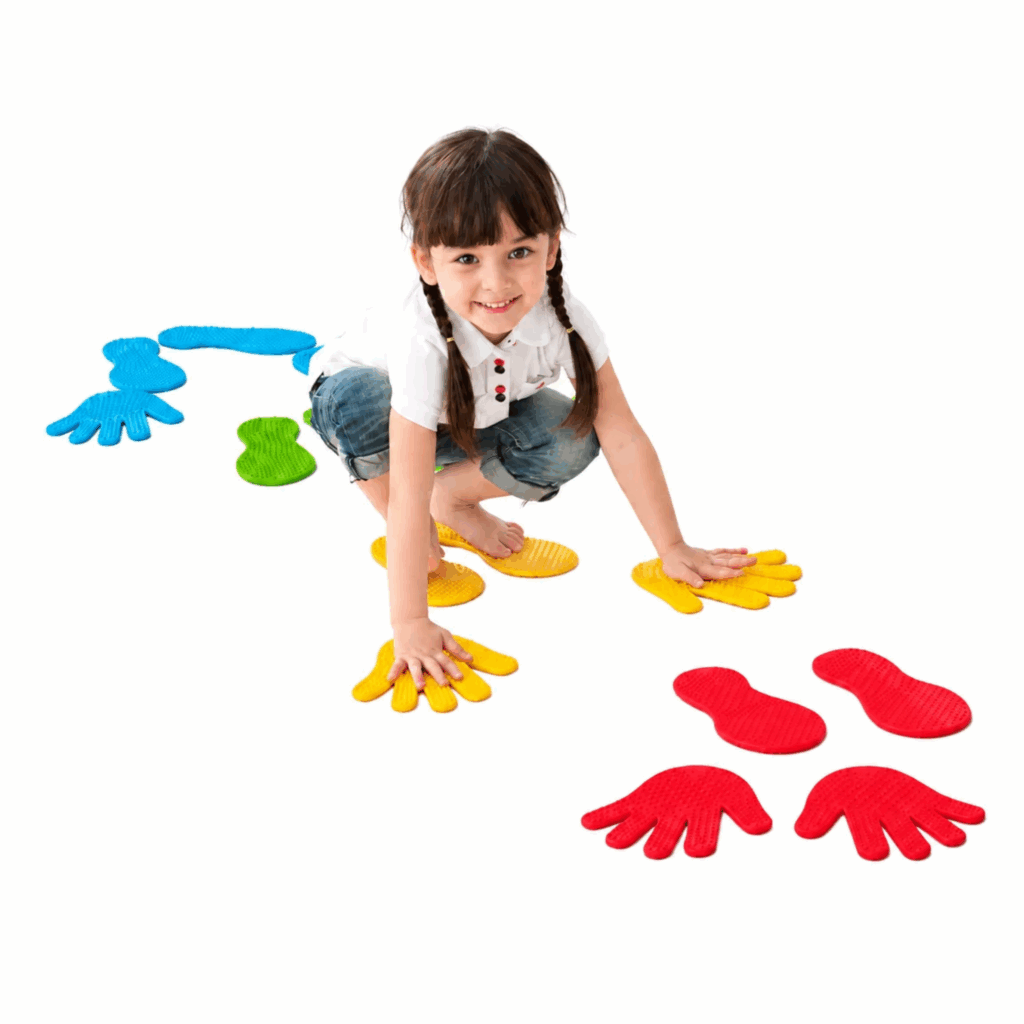 Ein Mädchen spielt mit bunten Hand- und Fußmatten auf einem weißen Hintergrund. Die Matten in Blau, Grün, Gelb und Rot fördern die Motorik und das Gleichgewicht von Kindern.