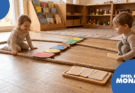 Zwei Kinder spielen im Innenraum mit bunten Formen auf einem Seil. Die Umgebung ist freundlich und einladend, mit Regalen voller Bücher und Spielzeug im Hintergrund. Das Bild zeigt eine kreative Lernumgebung, die die Fantasie und motorischen Fähigkeiten der Kinder fördert.