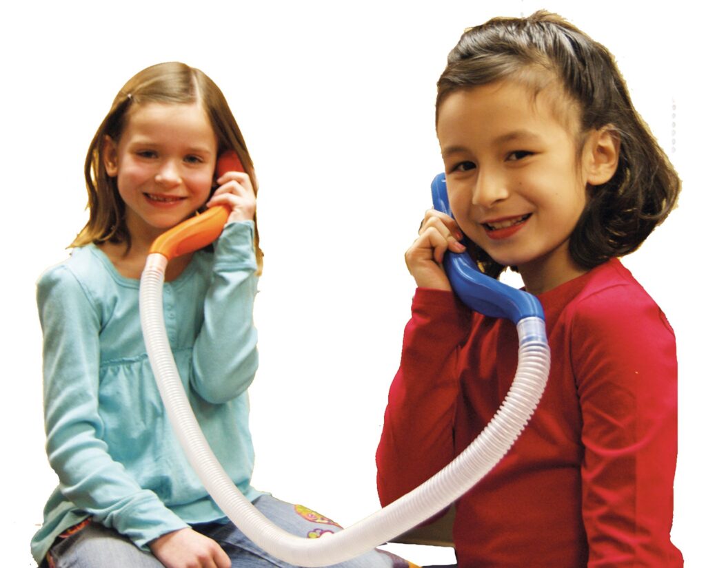 Zwei lächelnde Mädchen telefonieren miteinander, während sie bunte Telefone in den Händen halten. Das Bild zeigt eine spielerische Interaktion und fördert die Kommunikation im Kindesalter.